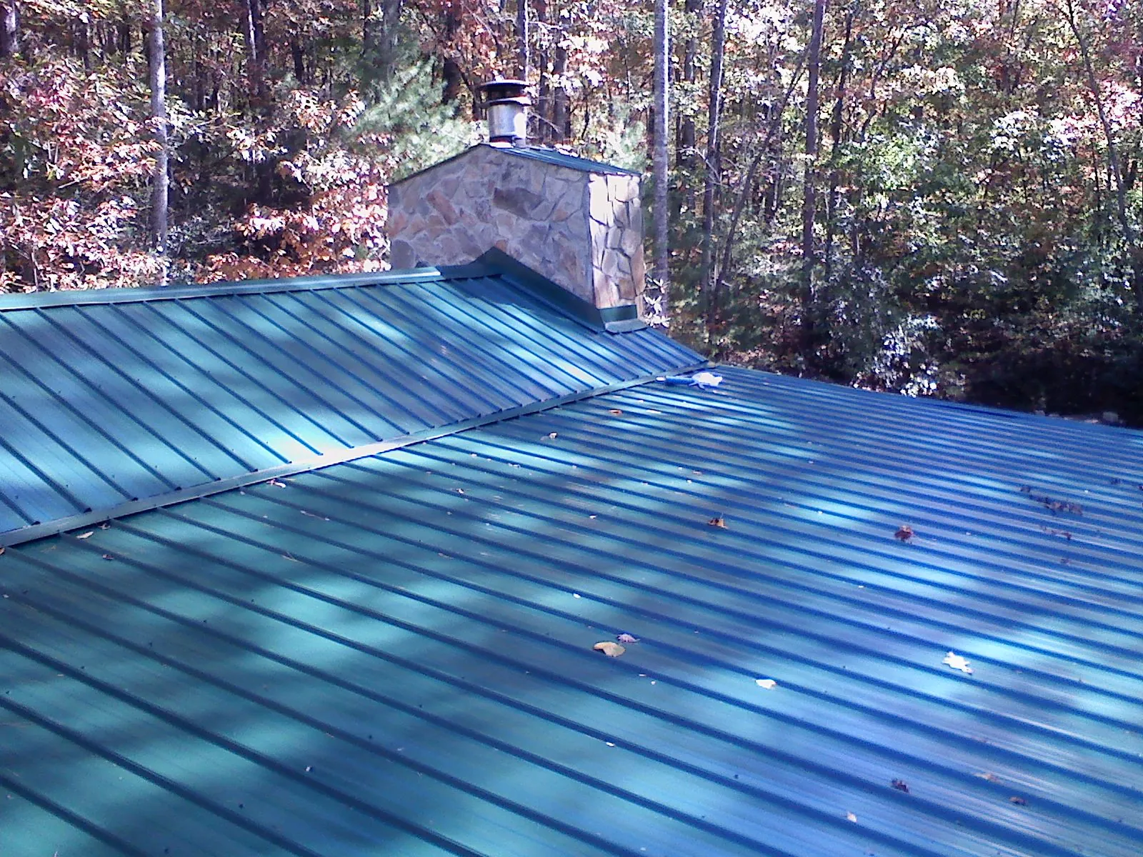 New green metal roof and stone chimney surrounded by autumn woods in Syracuse
