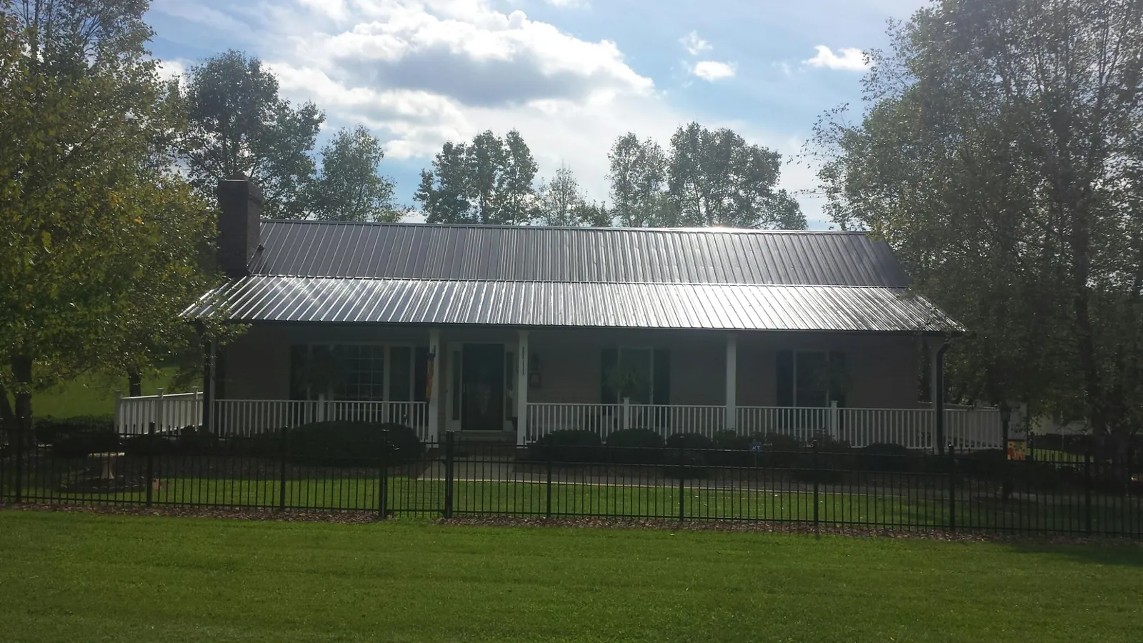 Gray metal roof on a brick ranch with a full width front porch — Gutter Guard Installation work by our crew in Syracuse